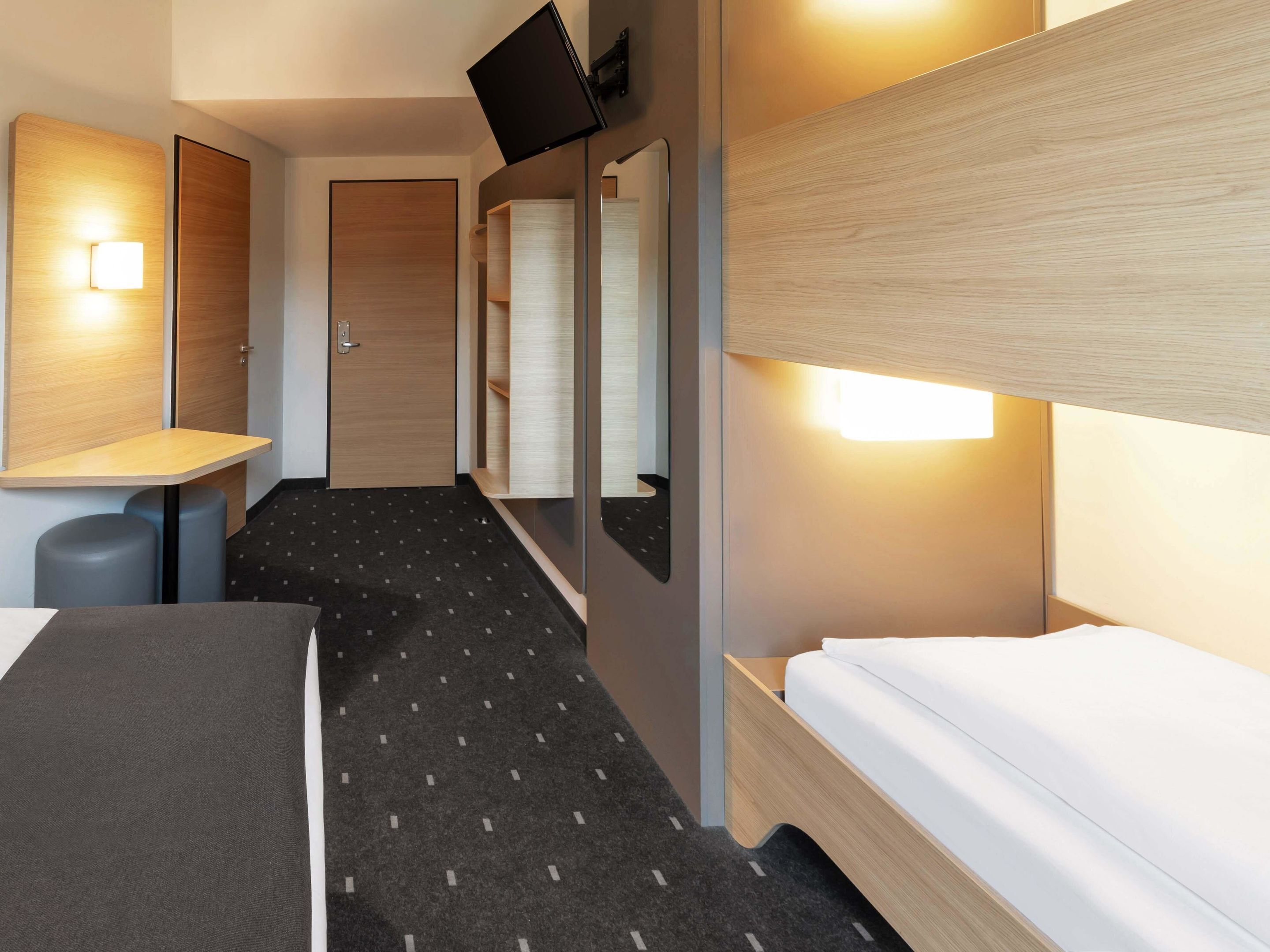 Ein Hotelzimmer mit Bett, Schreibtisch, Stuhl, Spiegel und Fernseher.