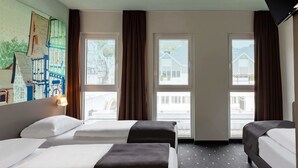 A hotel room with two beds, a wooden desk, and a large window with curtains.