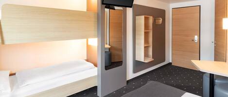 A modern hotel room with a bunk bed, a flat-screen TV, a small table, and a built-in shelf unit.