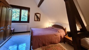 Une chambre à coucher avec un lit, une table de chevet, une commode, une fenêtre et un radiateur.