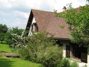A traditional house with a sloped roof, surrounded by lush greenery and flowering plants. - "Charmant Gîte Campagnard Proche Nancy – Nature, Confort et Activités ! " (Thélod)