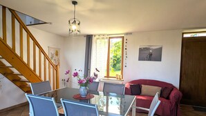 Un comedor con una mesa de vidrio, cuatro sillas, un jarrón con flores, una escalera de madera y un sofá rojo.