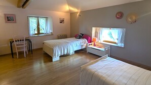 Un dormitorio con dos camas, un escritorio y una silla. Hay ventanas con cortinas, un radiador y una lámpara fijada a la pared.