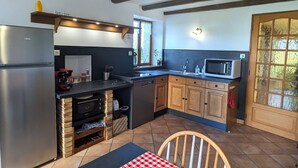 Cocina compacta con refrigerador, microondas y horno empotrado. Tiene gabinetes de madera, una ventana y una puerta con paneles de vidrio esmerilado.