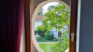 Una habitación con un ventanal circular que muestra un edificio de piedra y vegetación al exterior.