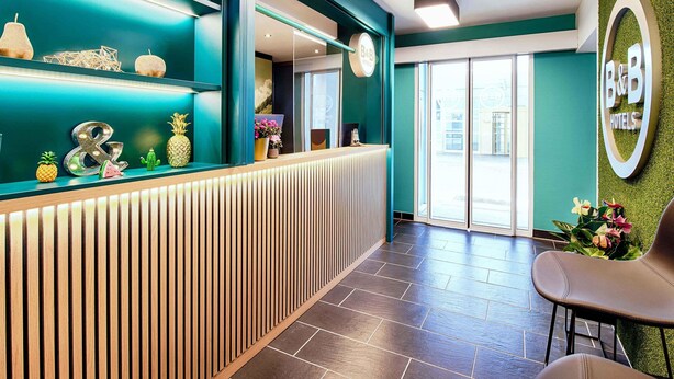 Un área de recepción con una decoración en tonos aguamarina, un mostrador de madera y el logotipo de B&B en la pared.