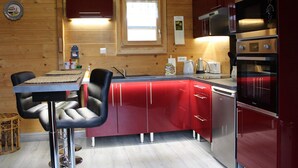Une cuisine compacte aux murs en bois, dotée d’un plan de travail rouge, d’un four encastré et d’une fenêtre située au-dessus de l’évier.