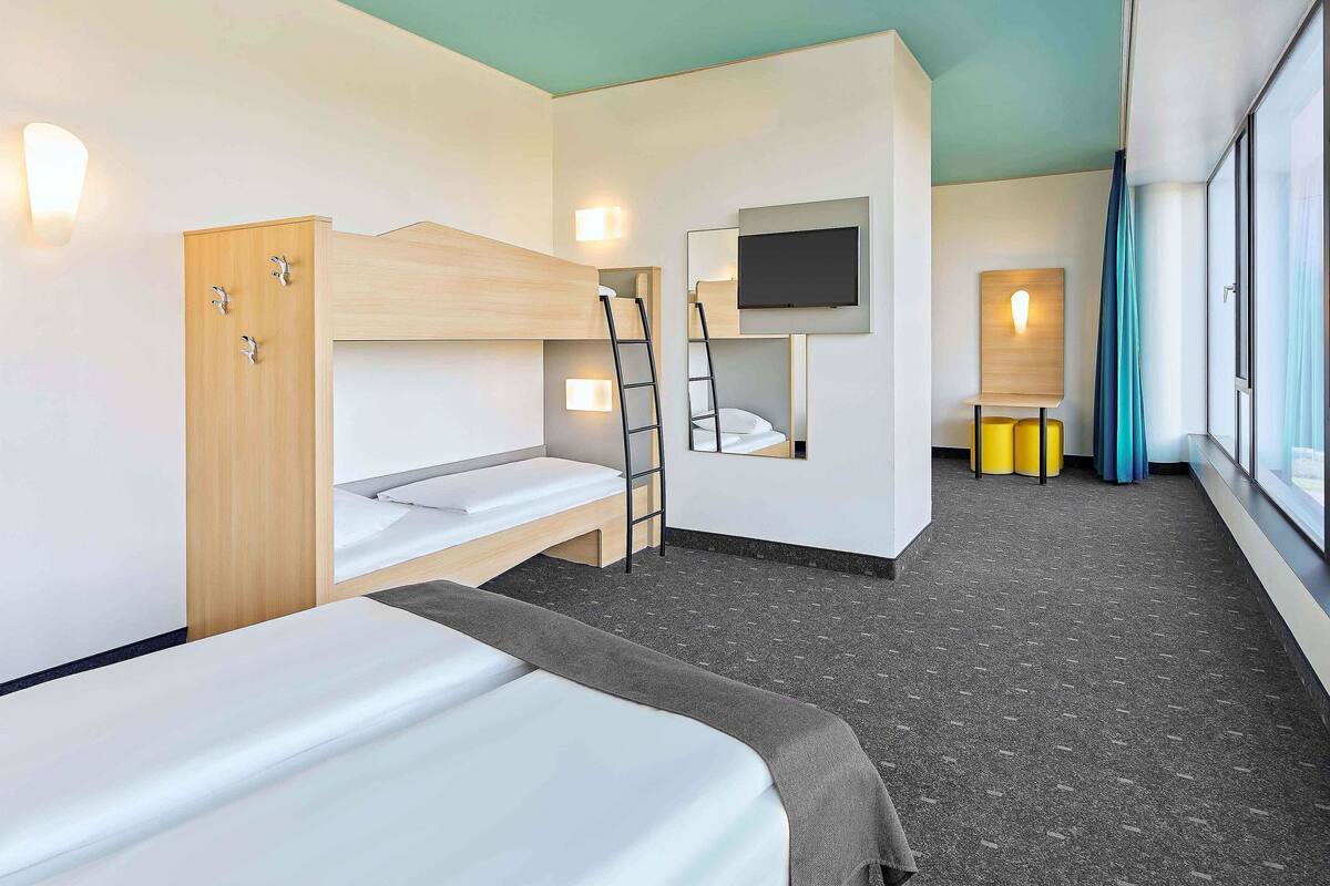 A modern hotel room with bunk beds, a TV, and a window with curtains.