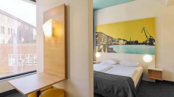 A hotel room with a bed, a desk, a chair, and a large window.