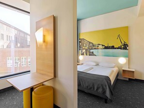 A hotel room with a bed, a desk, a chair, and a large window.