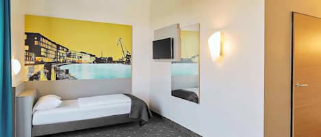 A hotel room with a bed, a wall-mounted TV, a mirror, and a painting of a cityscape.