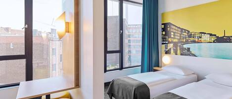 A hotel room with two beds, a desk, a chair, and a view of the cityscape.