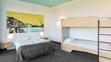 Quarto de hotel com uma cama, uma beliche, um quadro com vista urbana e uma mesinha de cabeceira.