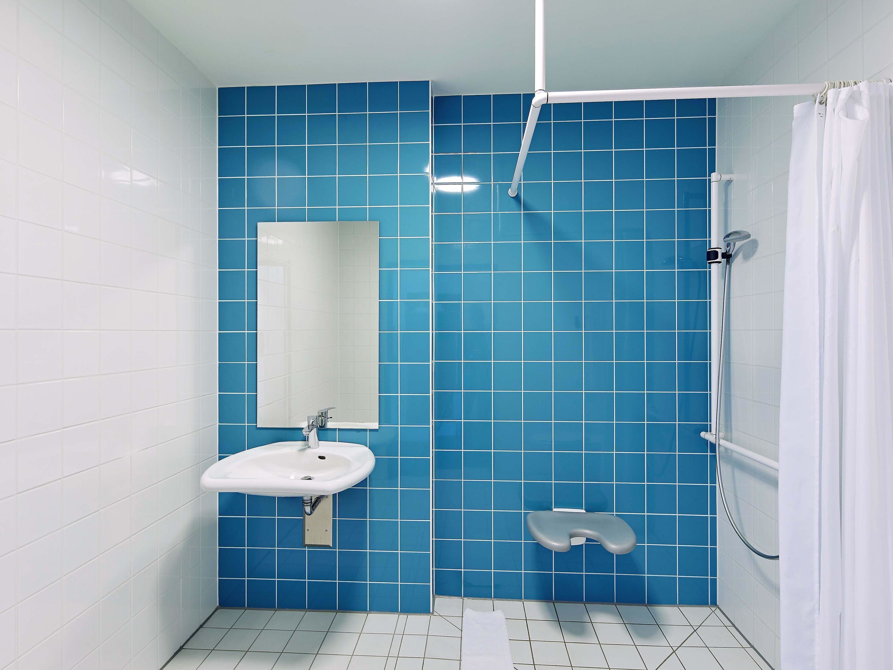 Baño con paredes de azulejos azules, un lavabo blanco, un espejo y una zona de ducha.