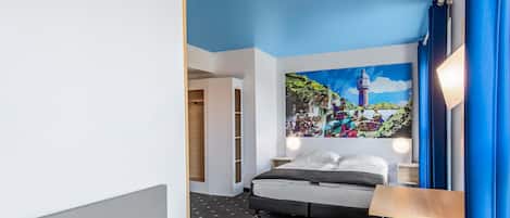 Una habitación de hotel moderna con una cama, un taburete verde, una mesita de noche y un mural en la pared.