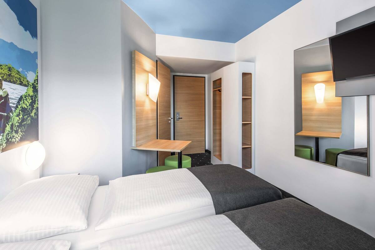 A hotel room with two beds, a wooden wardrobe, a mirror, and a TV.
