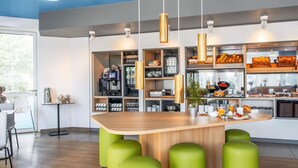 A modern kitchen with a central island, green stools, and various kitchen appliances. - B&B Hotel Neu-Ulm (Neu-Ulm)