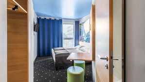 A compact room with a bed, a small table, and a green stool. - B&B Hotel Neu-Ulm (Neu-Ulm)