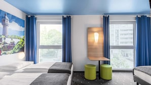A hotel room with two beds, a wall-mounted light, and a view of the city through large windows. - B&B Hotel Neu-Ulm (Neu-Ulm)