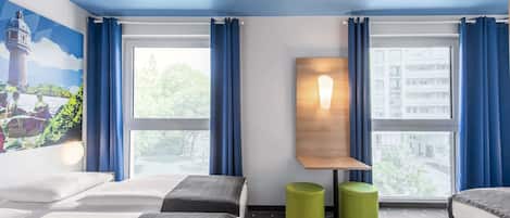 Habitación de hotel con dos camas, una lámpara fijada a la pared y vistas a la ciudad a través de amplias ventanas.
