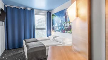 Habitación de hotel con cama, escritorio, silla, televisor y ventana con cortinas.