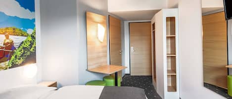 A modern hotel room with a bed, a desk, a wardrobe, and a large mirror.