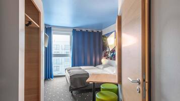 Una habitación de hotel pequeña con una cama, una mesita y dos taburetes verdes.