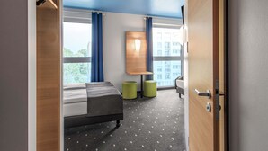 A modern hotel room with a bed, a desk, two green stools, and large windows offering a city view. - B&B Hotel Neu-Ulm (Neu-Ulm)