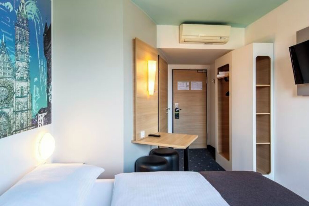 Een hotelkamer met een bed, nachtkastje en een klein bureau.