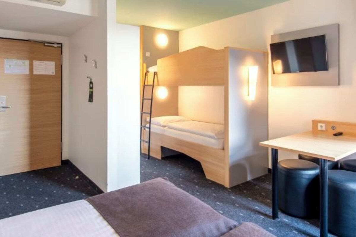 Een kleine hotelkamer met een stapelbed, een bureau en een aan de muur bevestigde televisie.