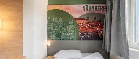 A hotel room with a bed, a nightstand, a wall-mounted lamp, and a cityscape mural.