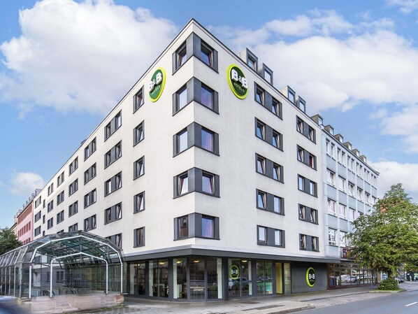 Un hotel tipo B&B moderno con fachada de vidrio, varios pisos y cielo despejado.