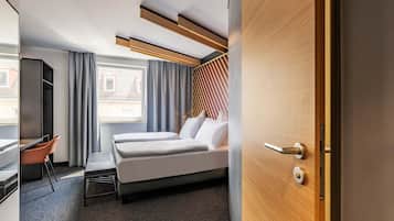 A modern hotel room with a bed, a desk, and a view of the outside.