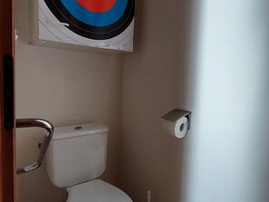 A small, narrow bathroom with a toilet, a paper towel dispenser, and a target on the wall. - Quiet house, 2 bedrooms, terrace, pets allowed, parking, EV charging (Velle-sur-Moselle)