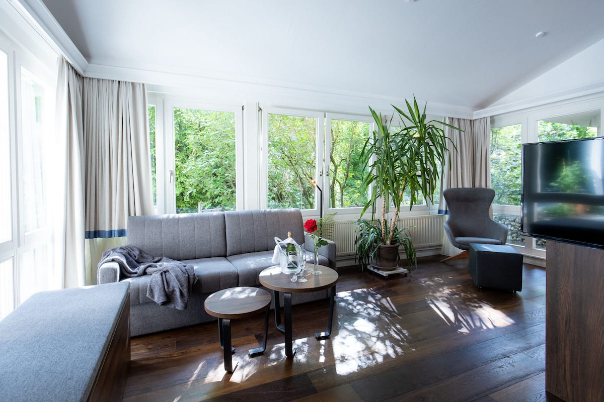 A modern living room with a grey sofa, a round coffee table, a TV, and a large window with curtains.