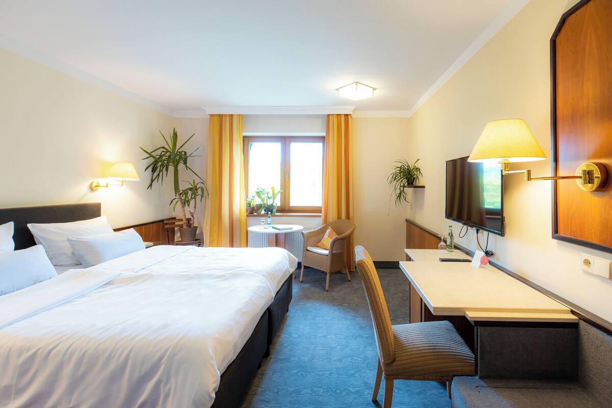 A hotel room with a large bed, a desk with a chair, a television, and a window with curtains.