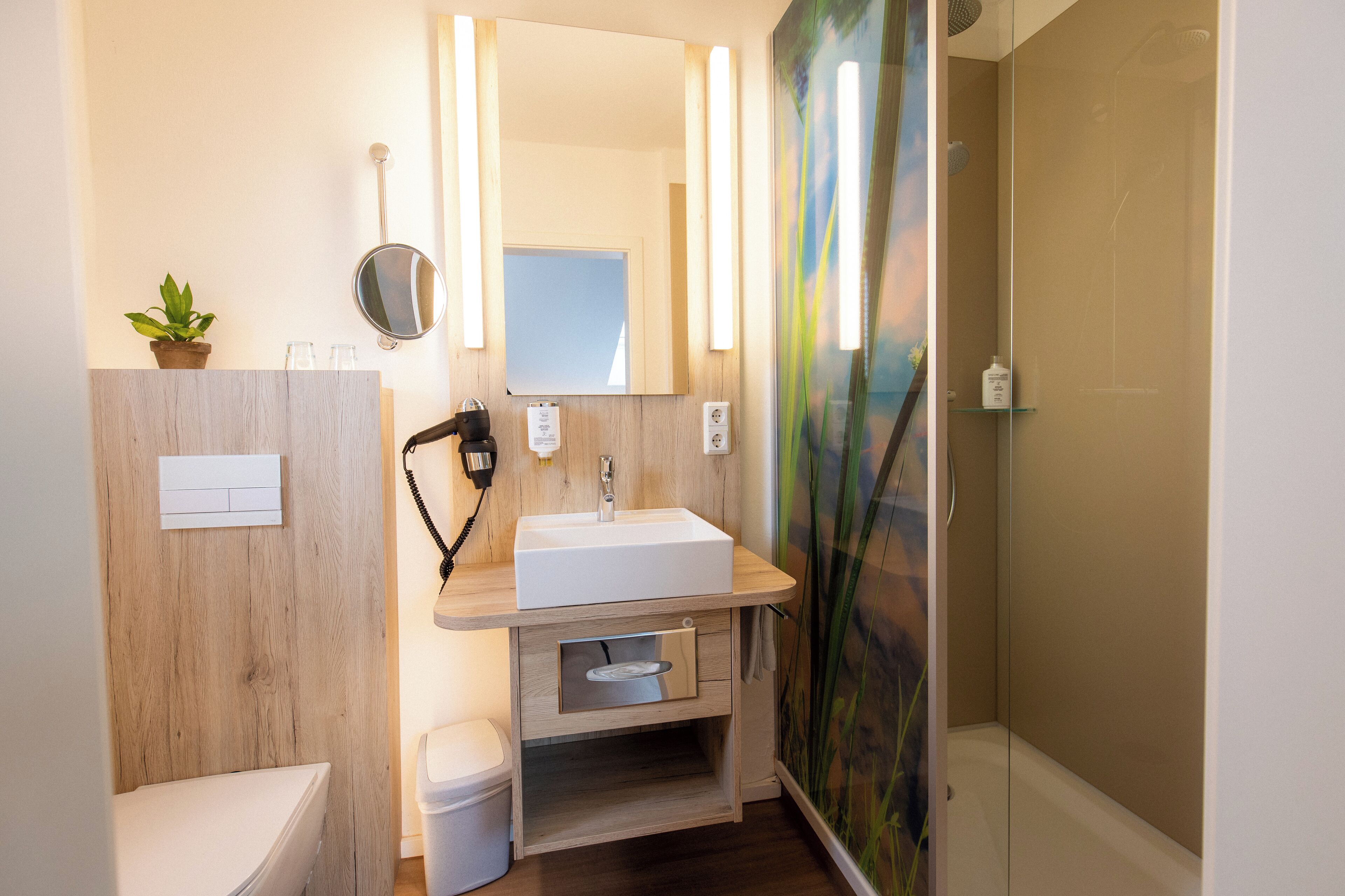 A modern bathroom with a wooden vanity, a white sink, a mirror, and a shower enclosure.