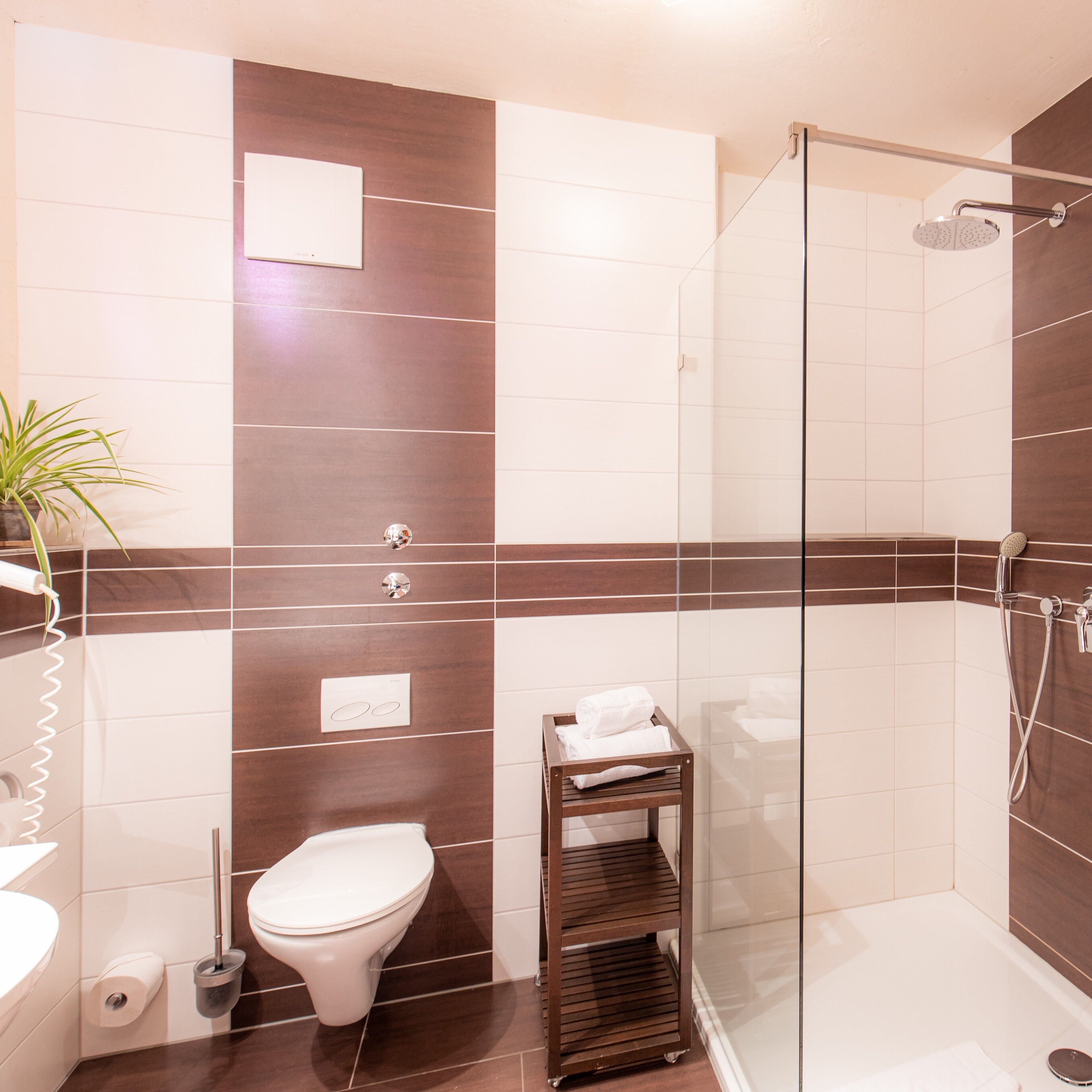 Ein modernes Badezimmer mit Duschkabine aus Glas, Toilette, Waschbecken und einer kleinen Ablage mit Handtüchern.