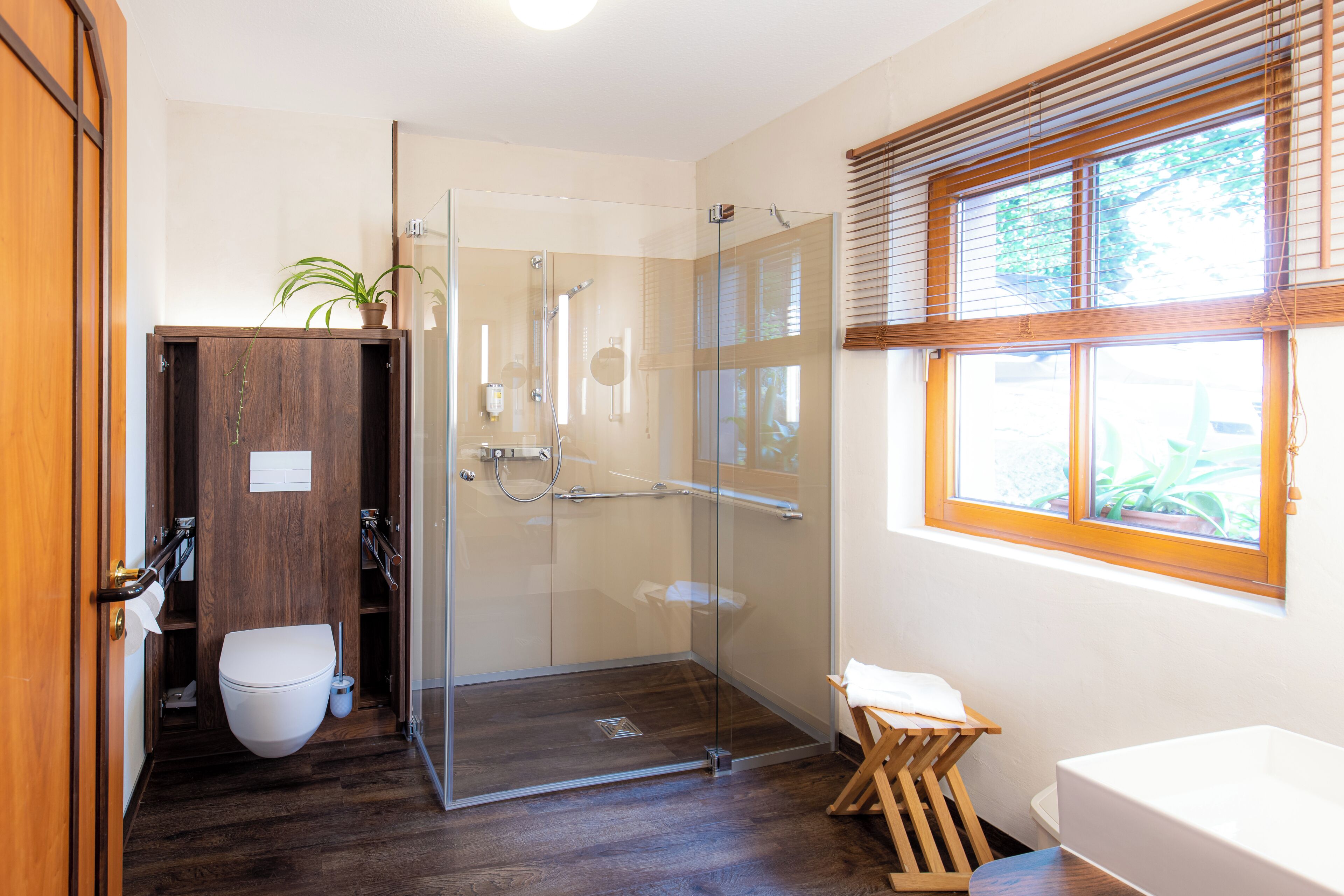 Un baño moderno con cabina de ducha de vidrio, tocador de madera y ventana con persianas.