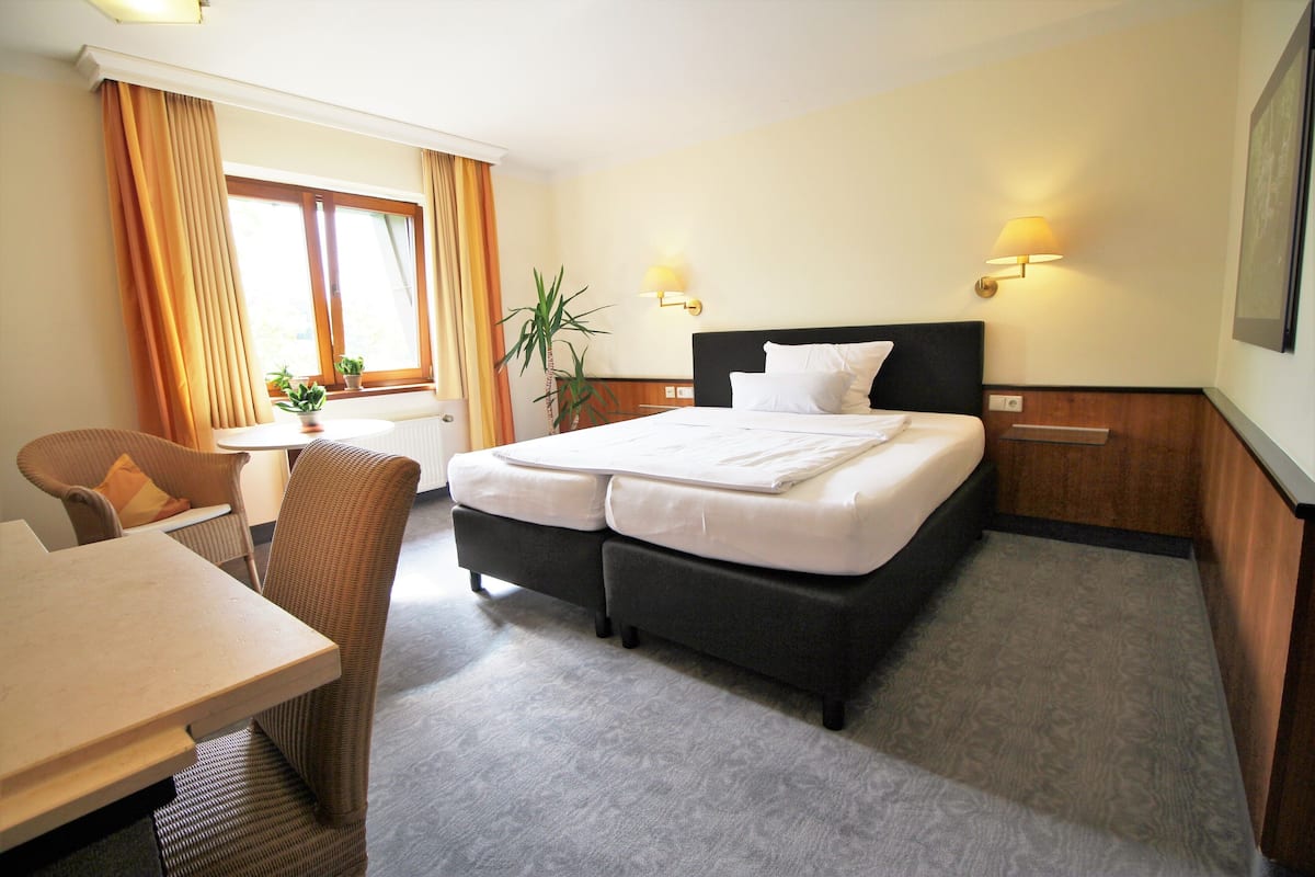 A hotel room with a bed, a desk, a chair, and two wall-mounted lamps.