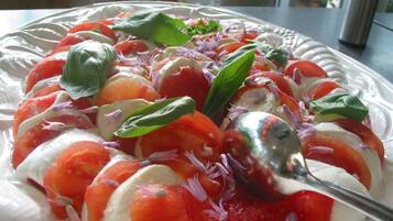A plate of Caprese salad with tomatoes, mozzarella, and basil, garnished with red onion and flowers.