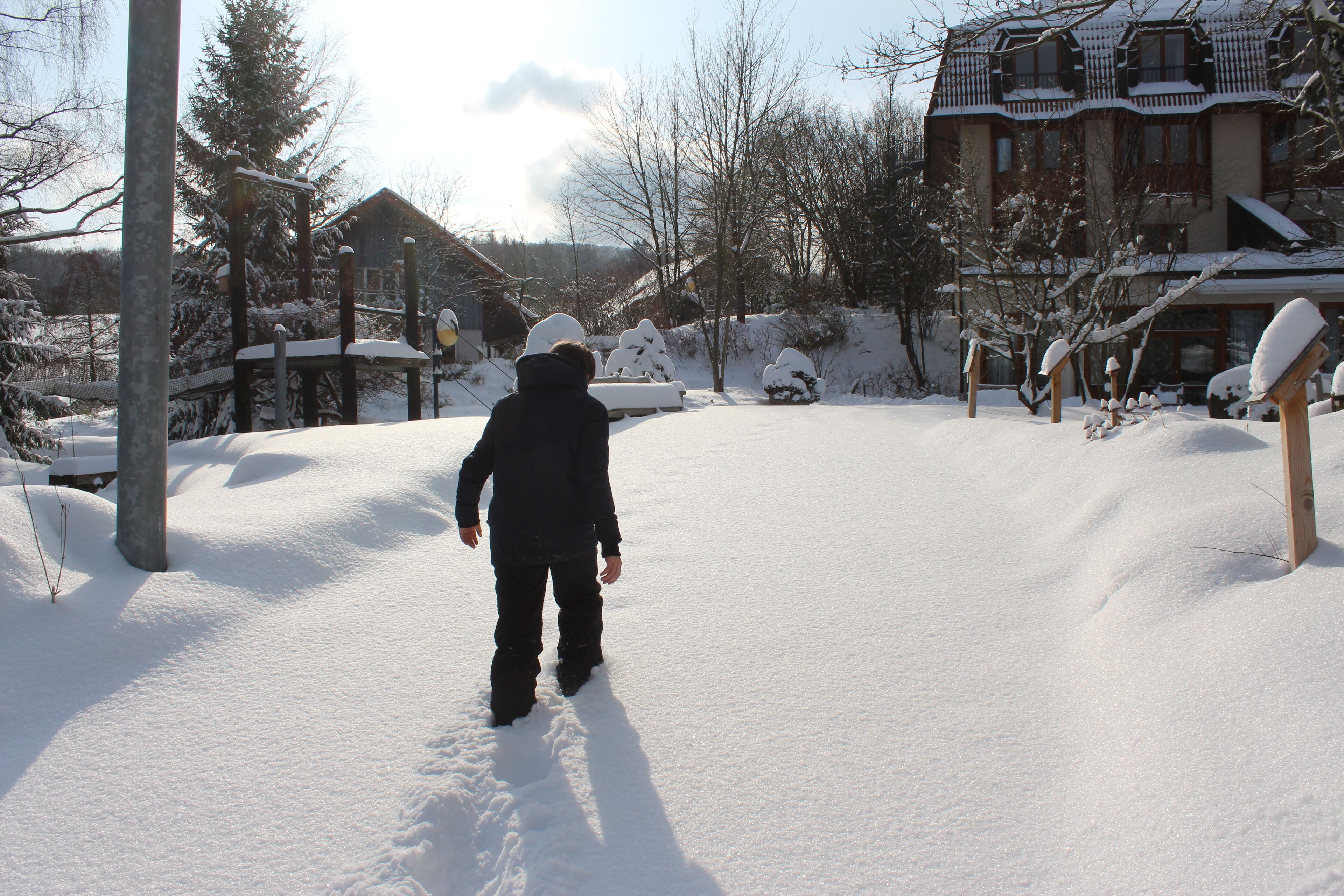 A person walking in a snow-covered area with buildings and trees in the background.