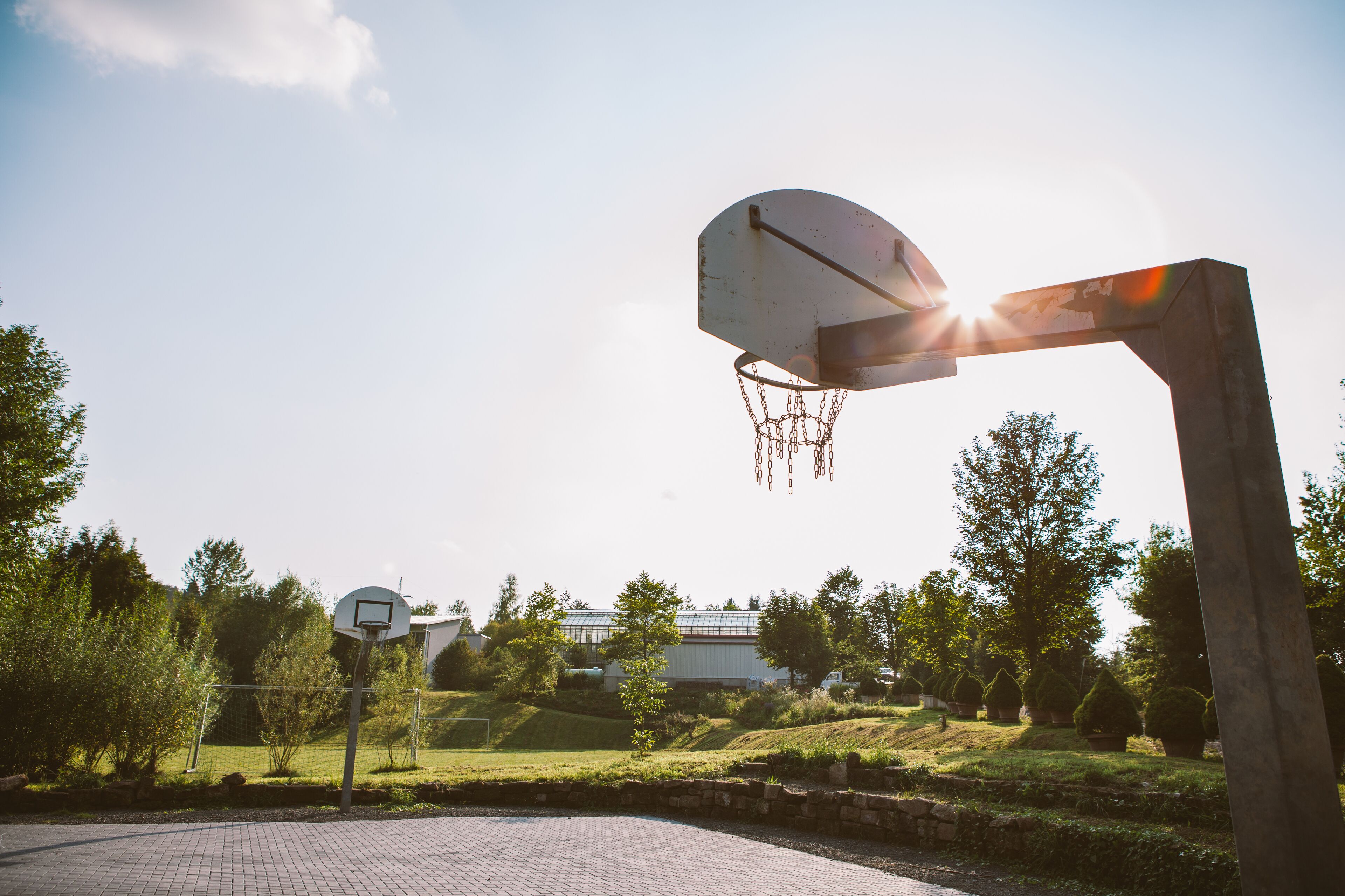 A basketball hoop in an outdoor setting with a clear sky and greenery in the background.