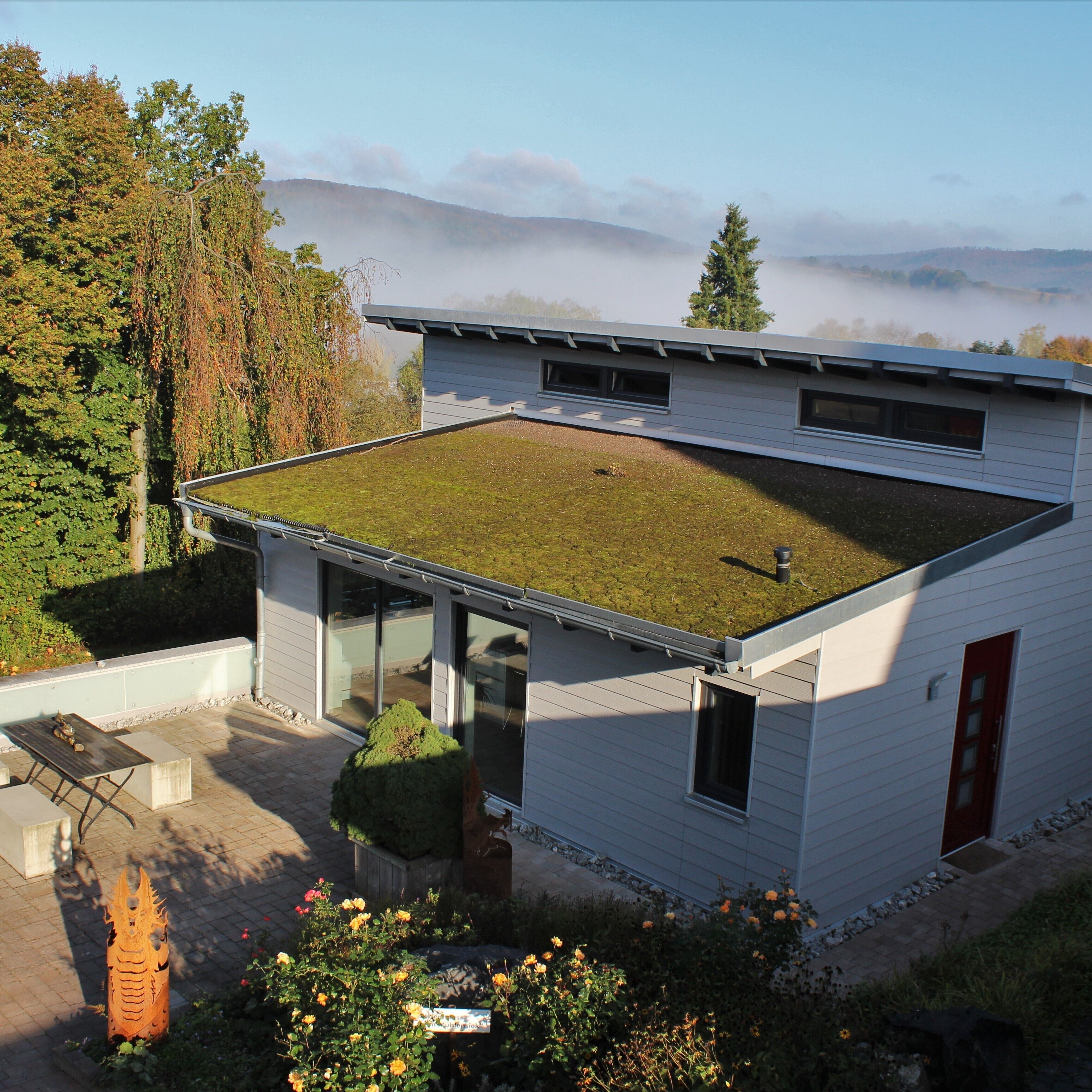 A modern house with a flat roof, large windows, and a small garden area.