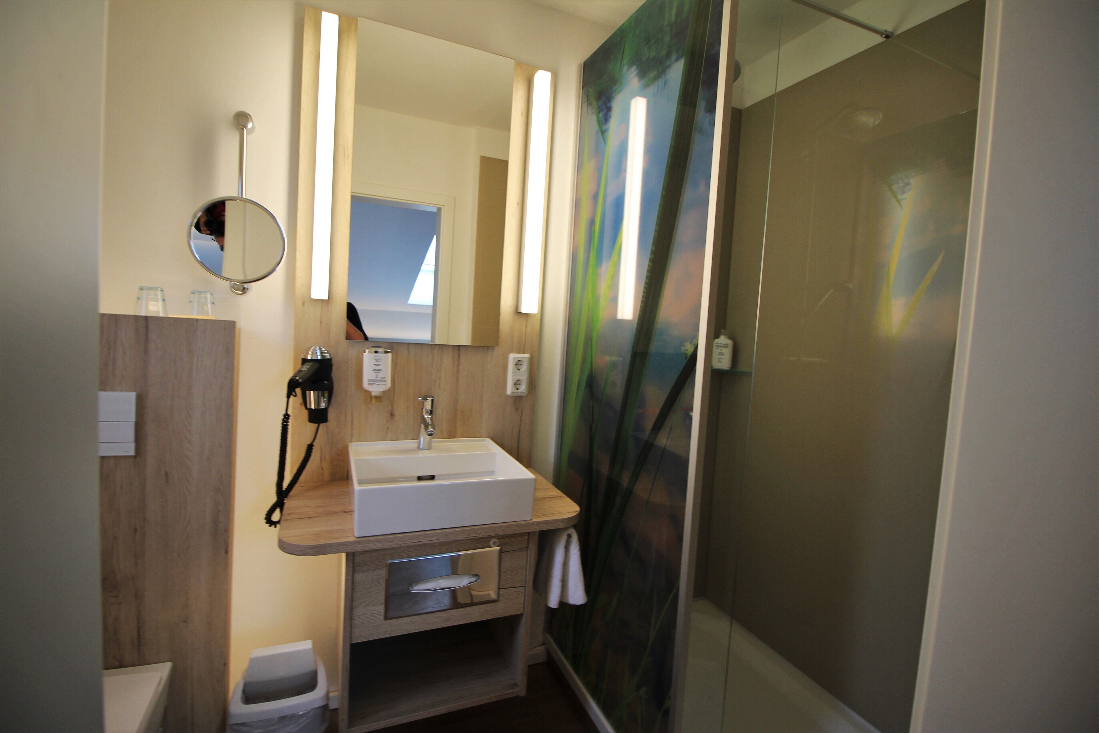 Ein Badezimmer mit einem Holzbadezimmerhocker, einem Waschbecken, einem Spiegel und einer Dusche mit Glastür.