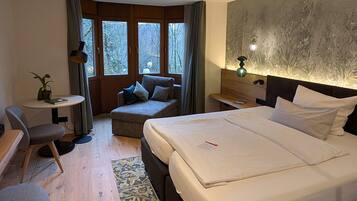 Habitación de hotel con una cama grande, un sofá pequeño, un escritorio y vistas a árboles a través de las ventanas.