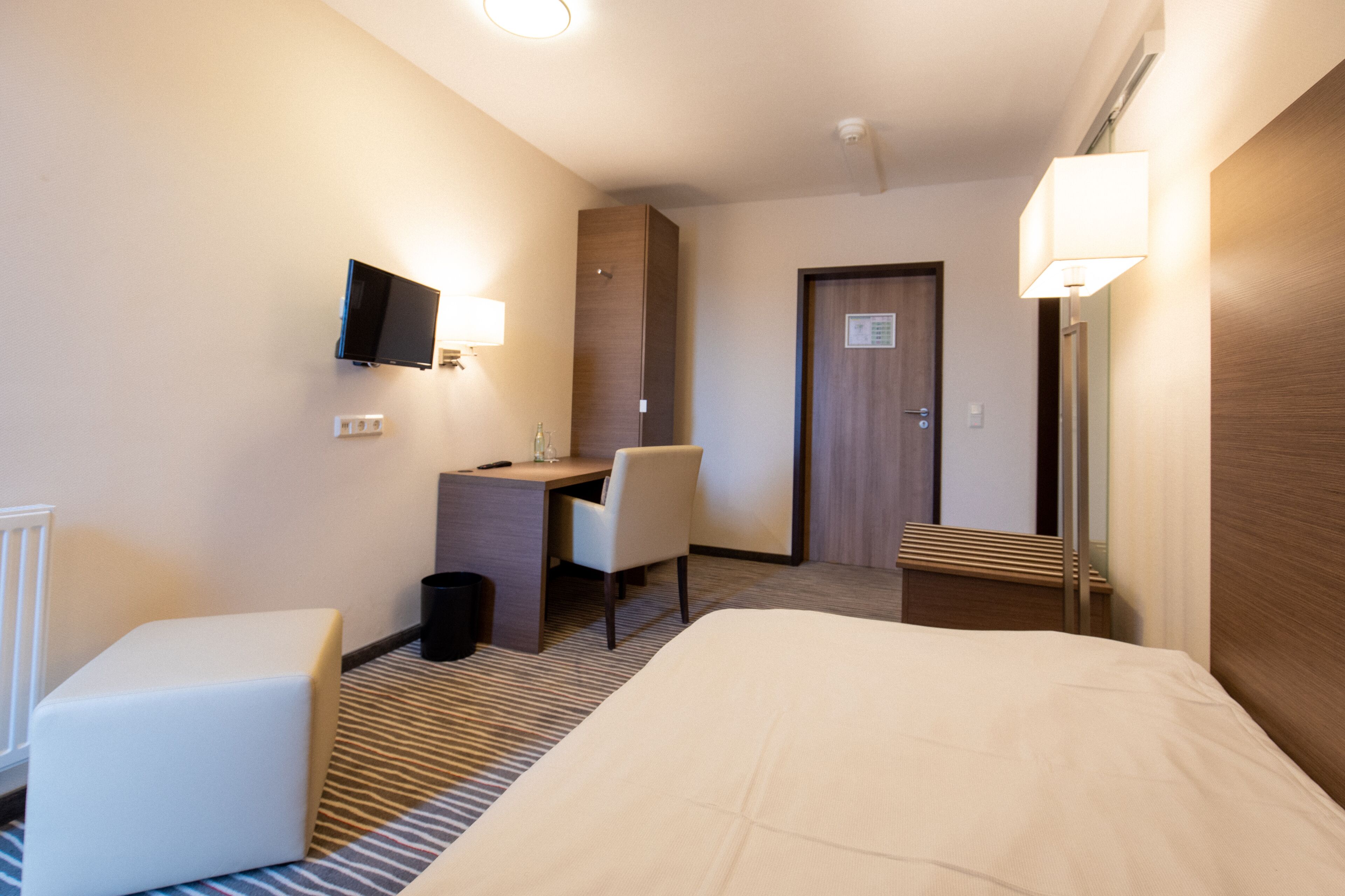 Una habitación de hotel con una cama, un escritorio, una silla, un televisor y un espejo.