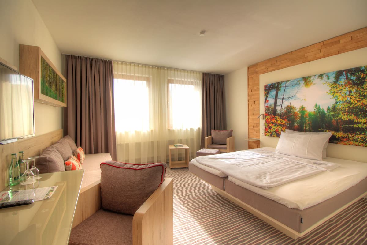 A hotel room with a bed, a desk, a chair, a small table, and a painting on the wall.