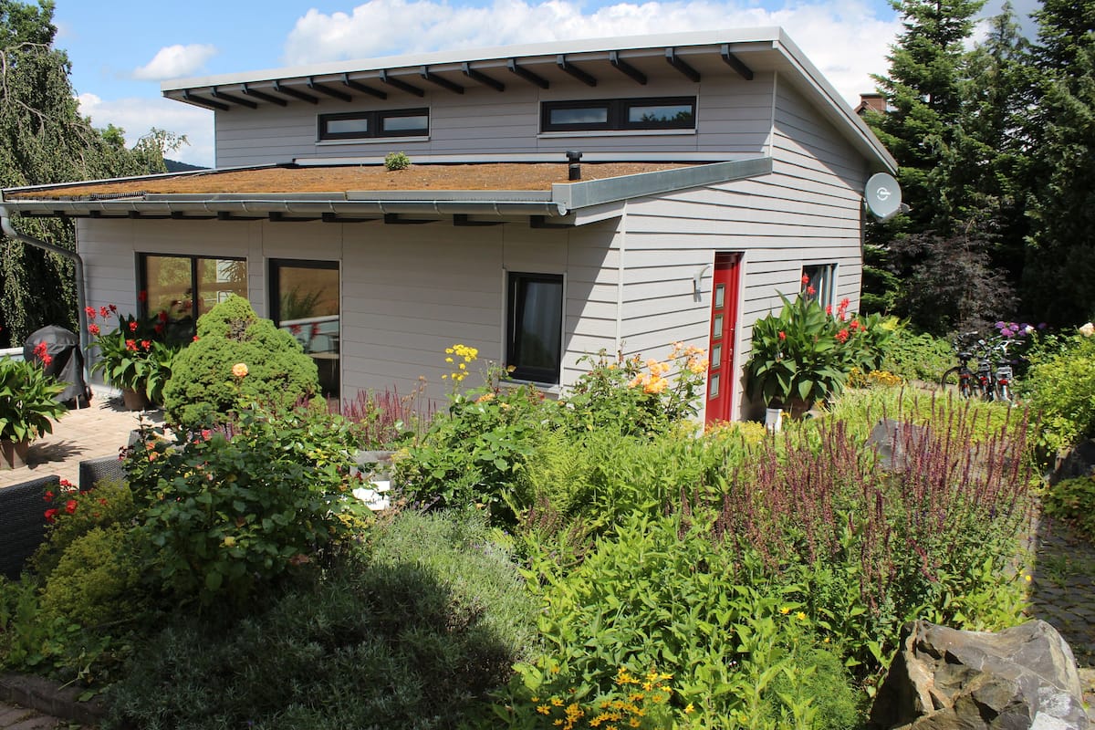 A modern house with a sloped roof, large windows, and a garden with various plants and flowers.