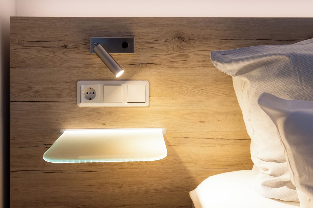A wooden headboard with a built-in light, a power outlet, and a bedside table.